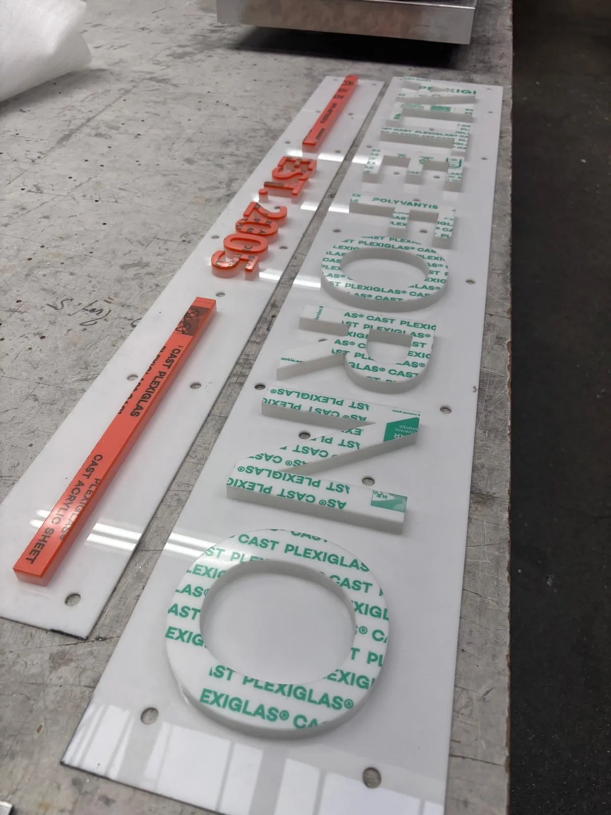 Weiße ALTE-FORNO-Acrylbuchstaben und orangefarbene Dekorelemente vor der Montage